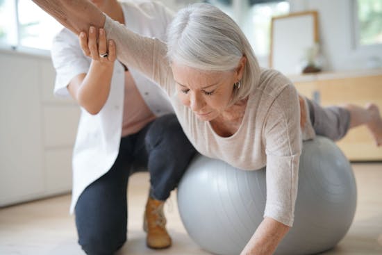 Older woman doing balance ball exercises with the aid of a physical therapist